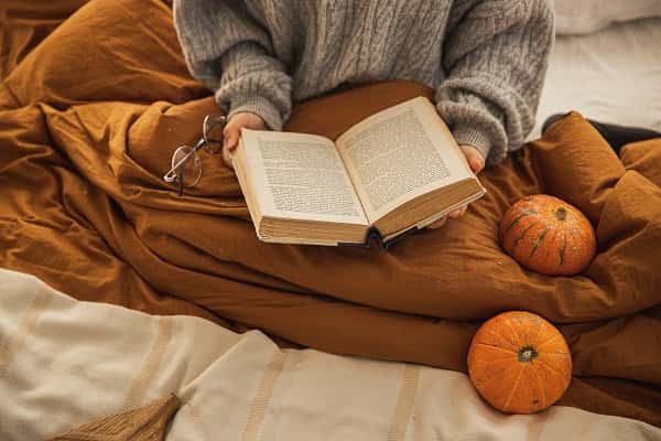 person in bed, reading a book, covered with a blanket